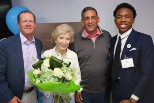 Group photo at an event featuring a woman with a white flower bouquet and a young man in a suit.