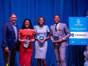Three Youth of the Year award winners holding trophies next to a presenter and event sign sponsored by Crowley.