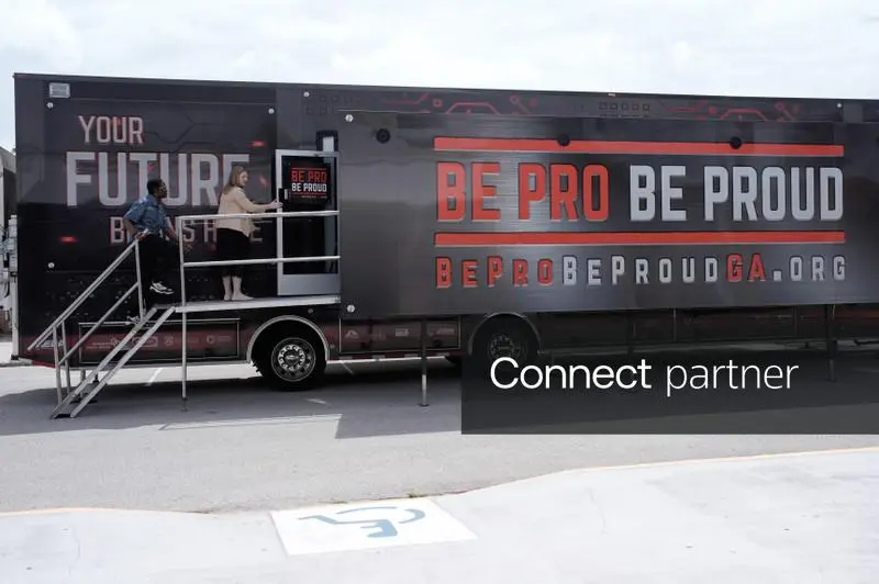 Two people entering a "Be Pro Be Proud" mobile workshop trailer parked outdoors.
